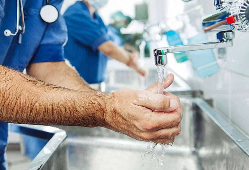 Healthcare worker washing hands at a clinical sink with faucet-mounted point-of-use filtration
